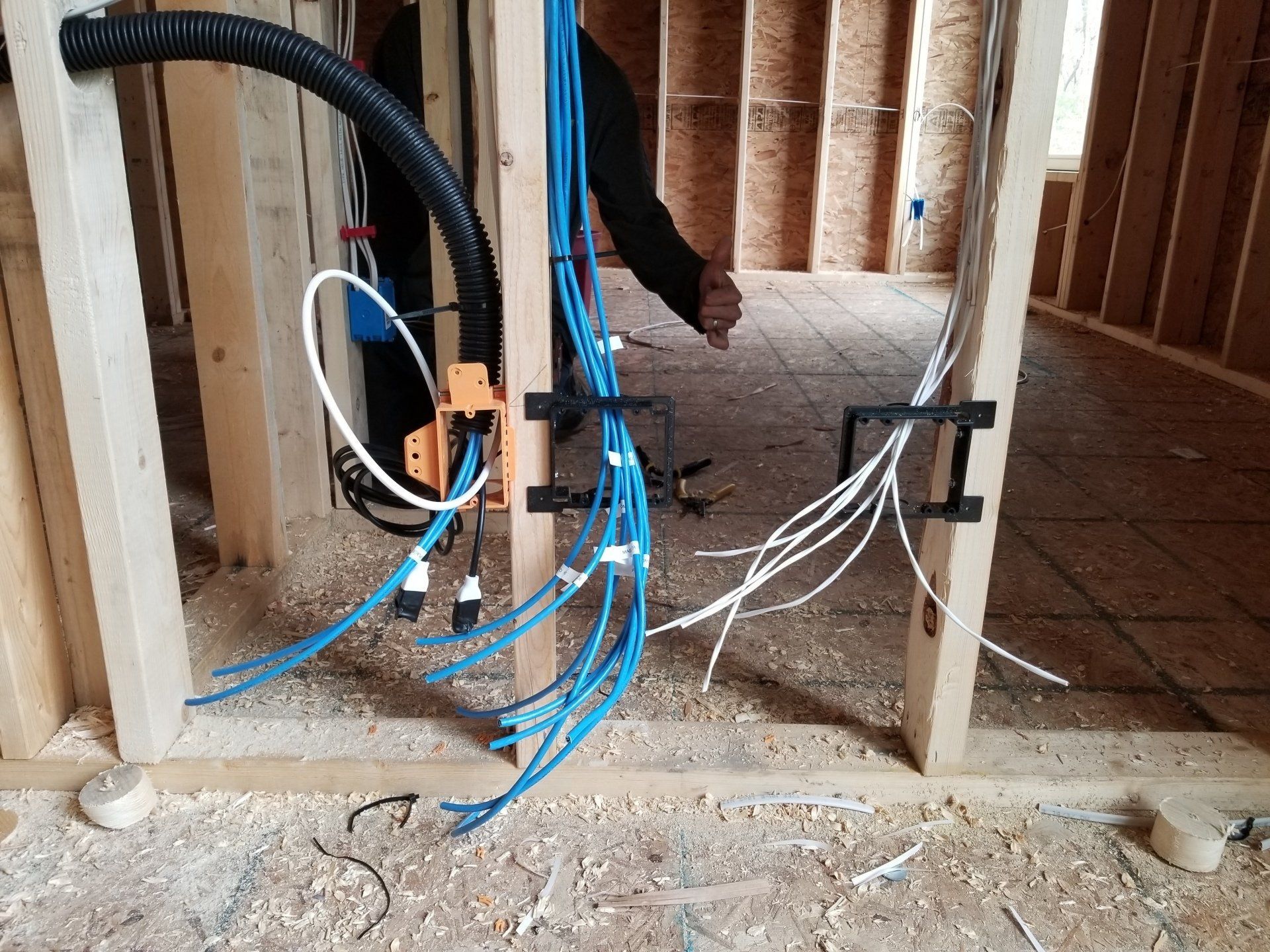 Network and speaker wiring in a wood-framed wall under construction; blue and white wires, black conduit.