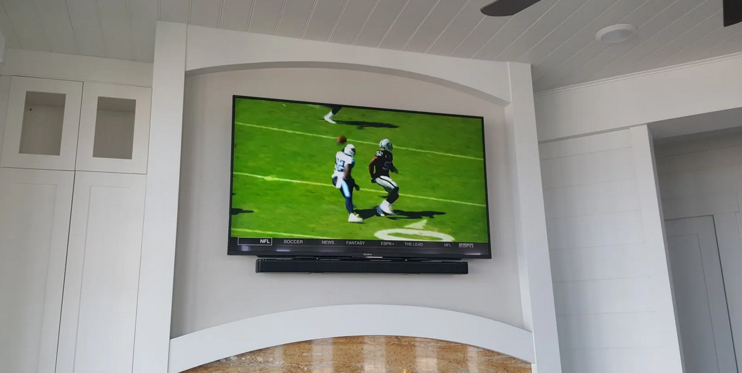 A TV and soundbar is custom mounted above a fireplace displays a football game.