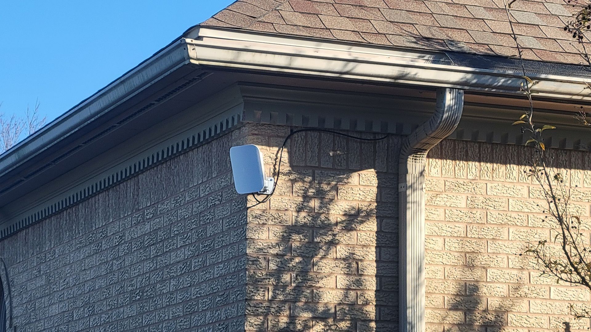 White rectangular device mounted on brick wall under a gutter.