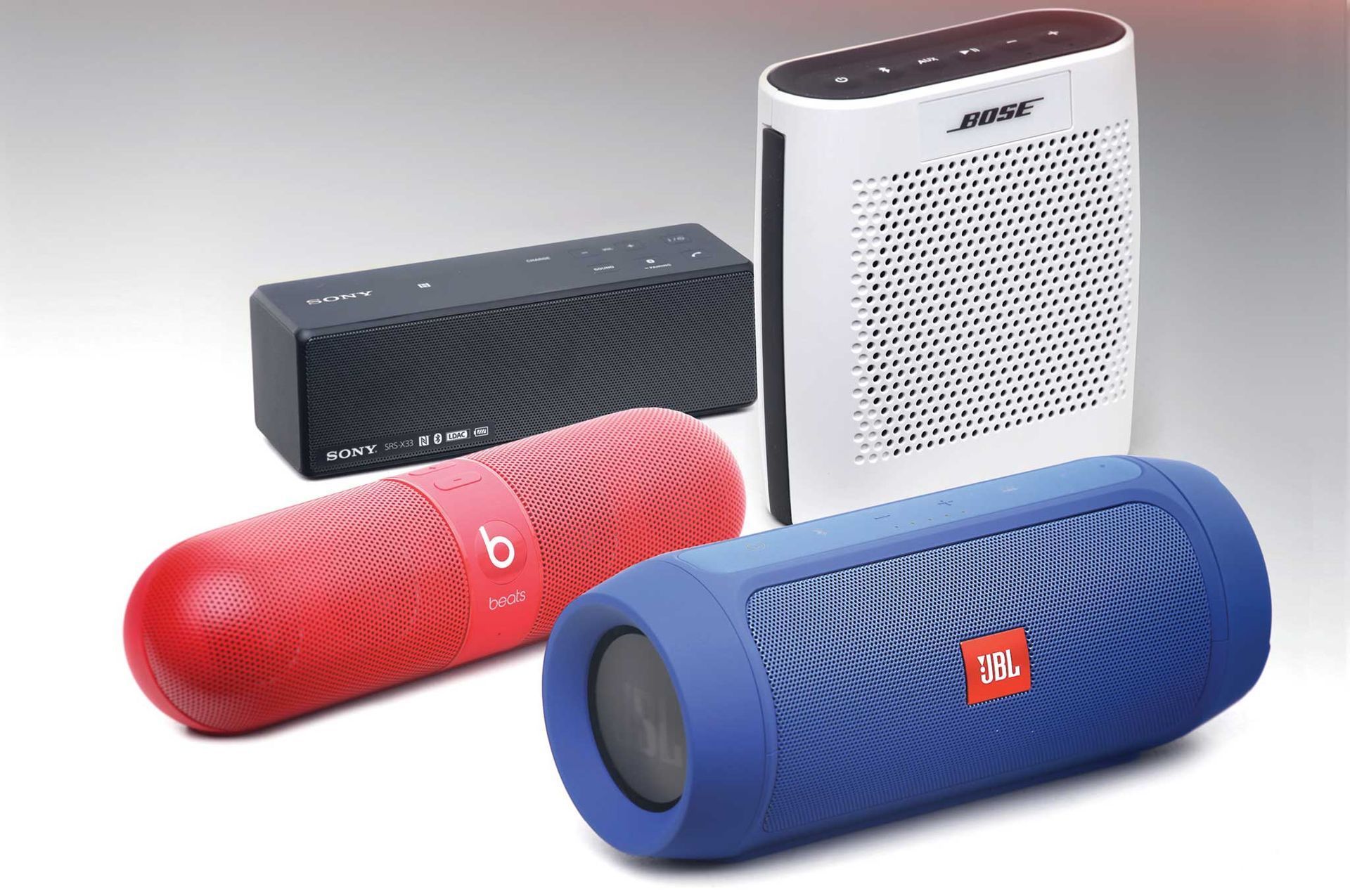 Bluetooth speakers in red, black, blue, and white, arranged on a light gray surface.