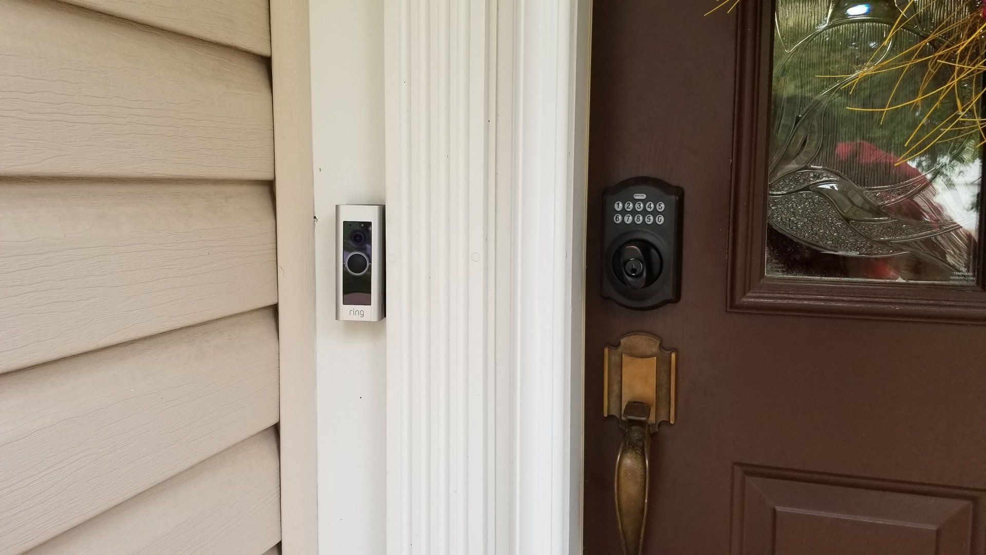 Ring doorbell on a white pillar next to a brown door with a smart lock and a glass window.