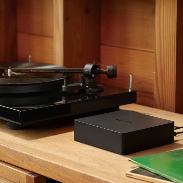 Black turntable and a sonos port on wooden surface; record albums nearby.