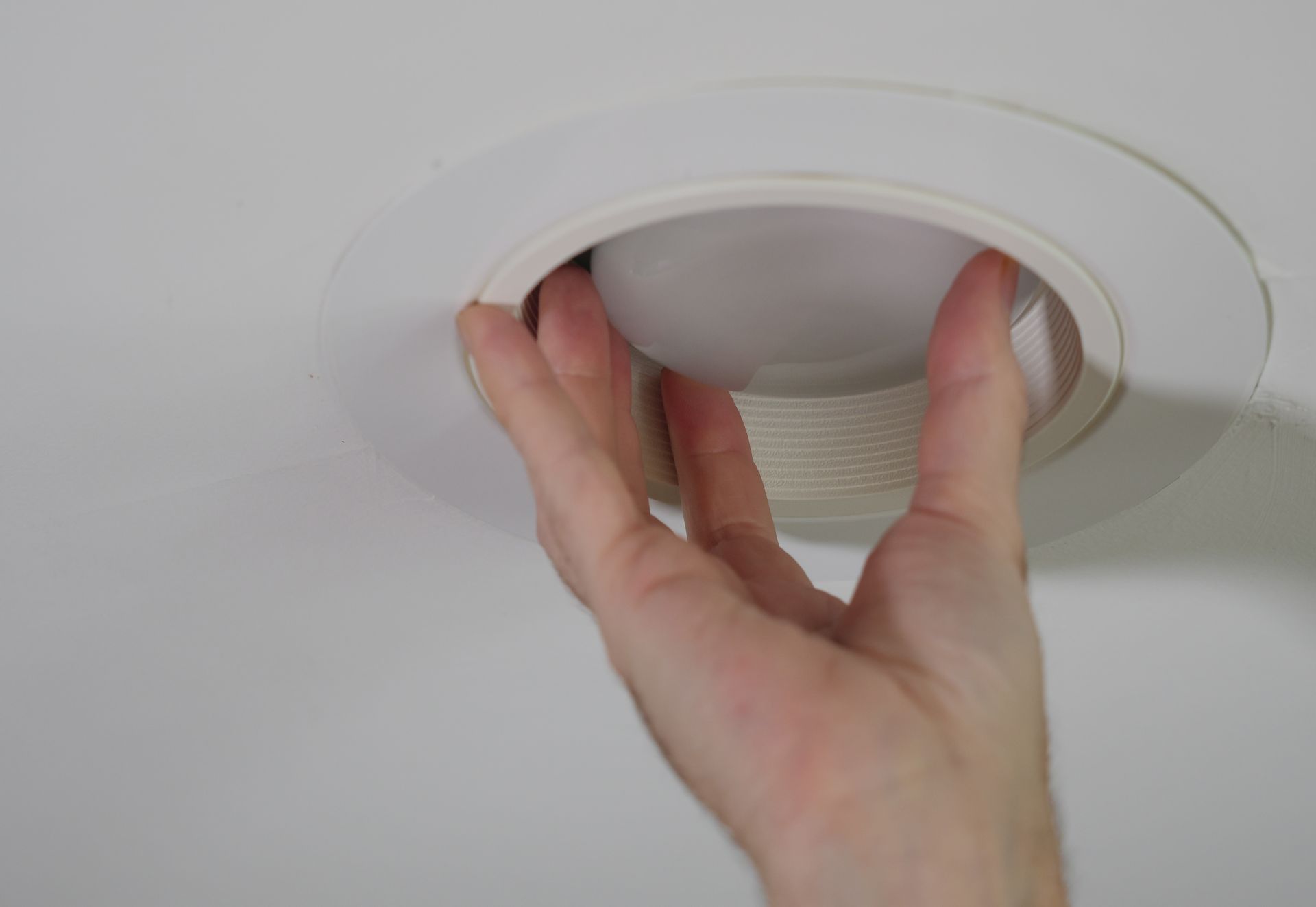 A skilled handyman installing a new light bulb in a recessed ceiling light fixture.