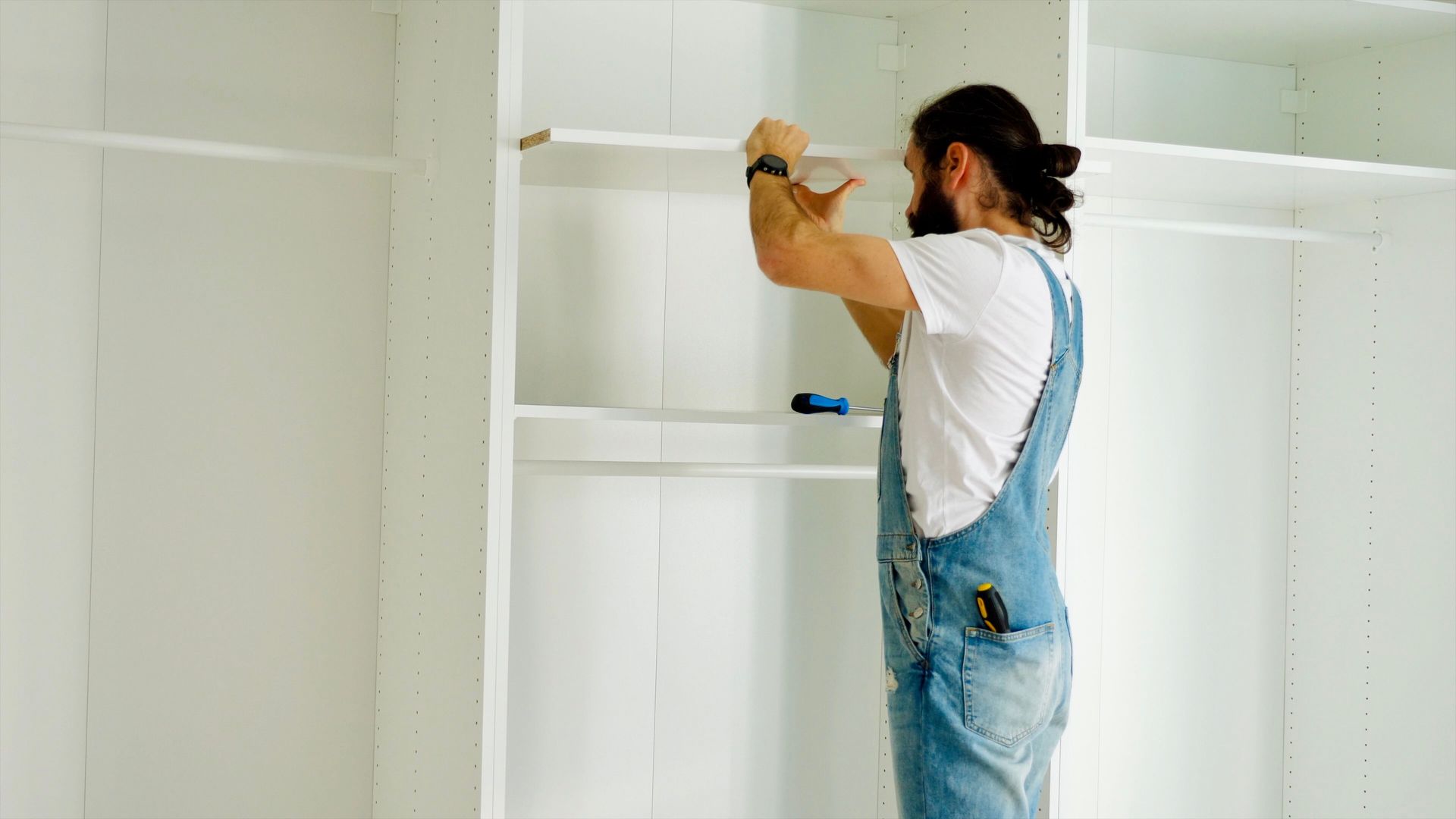 A handyman carefully installing a shelf inside a wardrobe during the furniture assembly process.