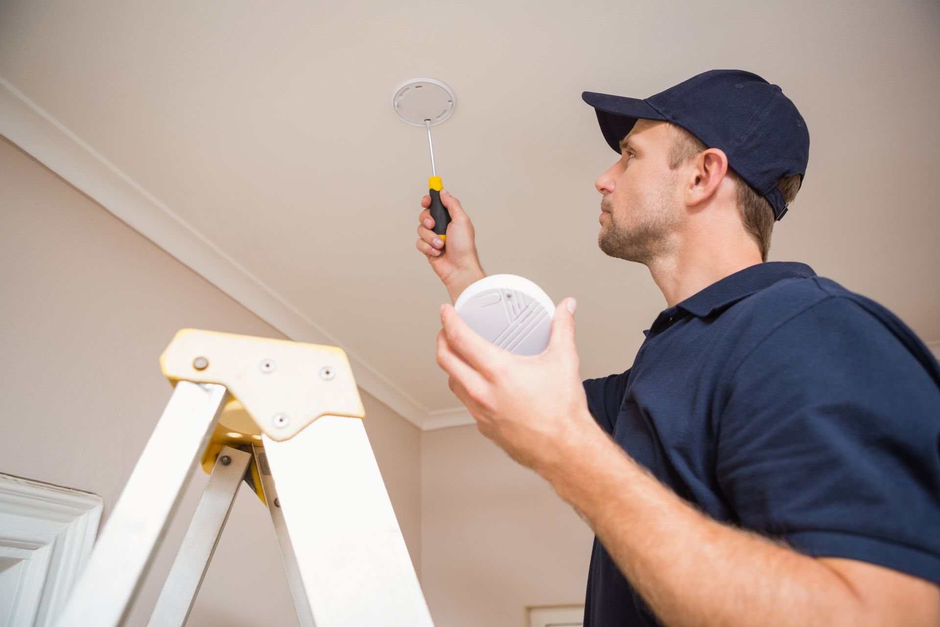 An individual installing a smoke detector on the ceiling of a room.