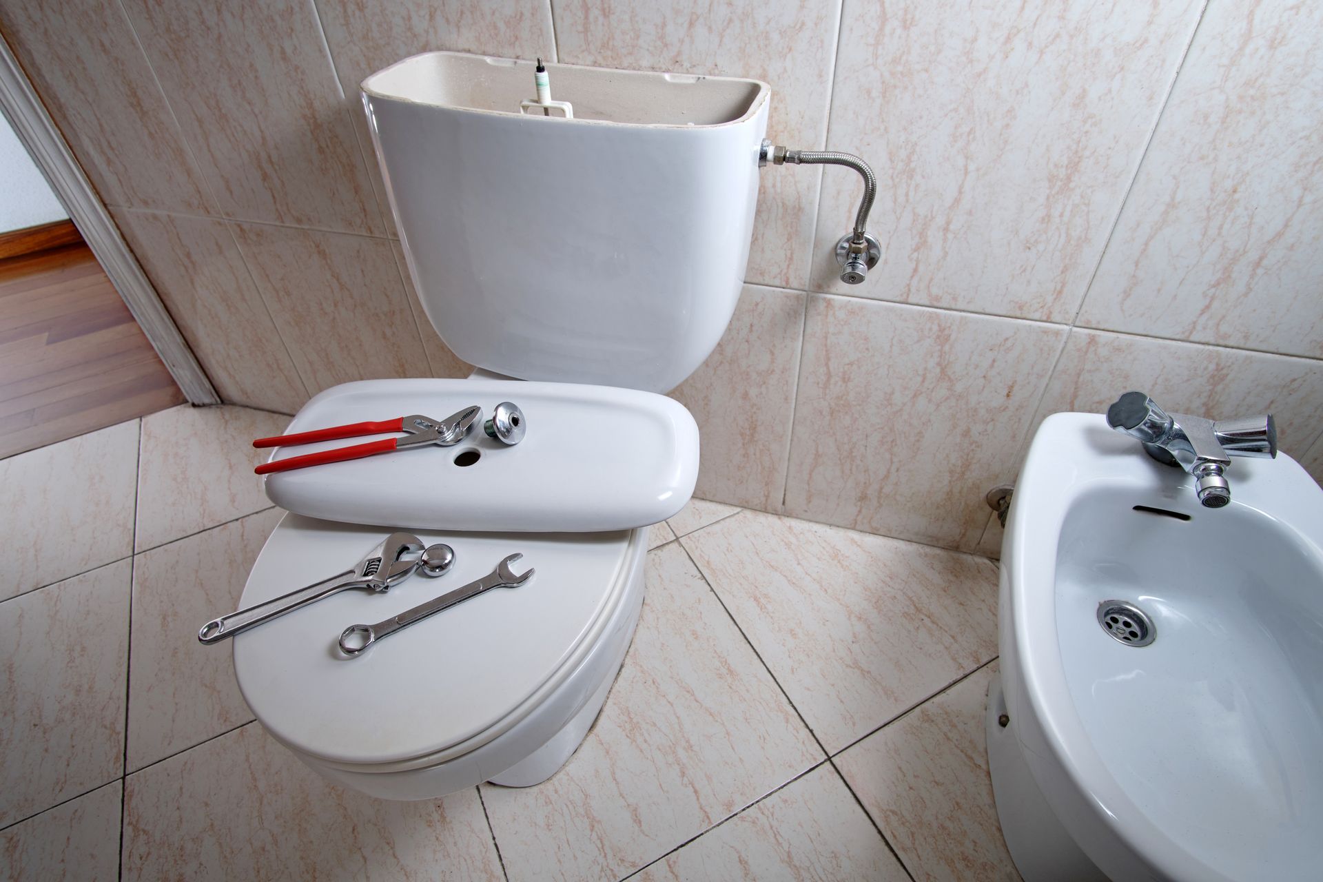 An open and damaged toilet cistern requiring repair. The lid is removed, revealing the inner components and exposed pipes.