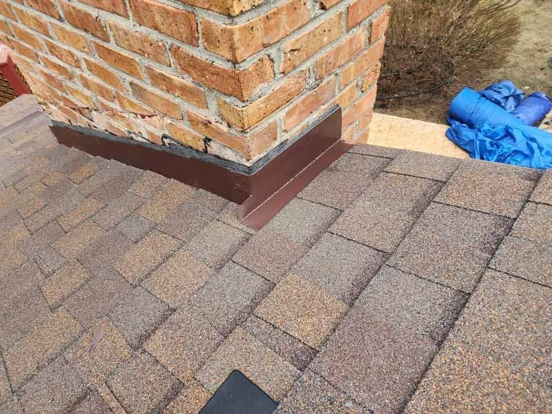 A brick chimney is sitting on top of a roof next to a brick wall.