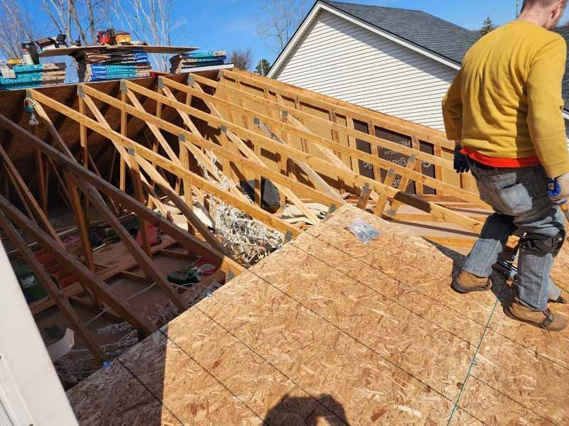 A man is standing on the roof of a house under construction.