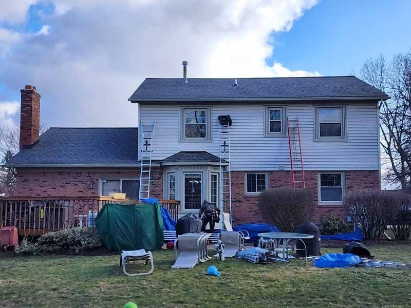 A house is being painted with a ladder in the backyard.