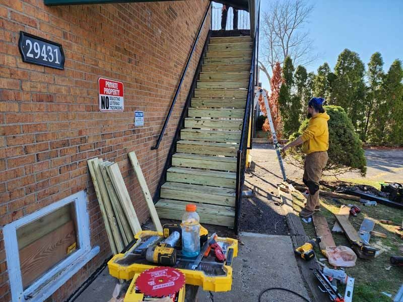 A man is working on a wooden staircase outside of a building.