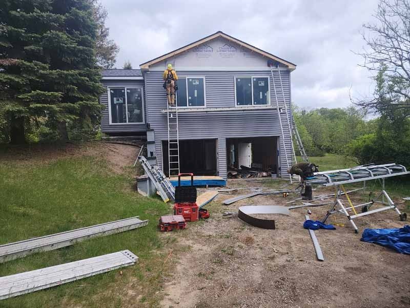 A man is standing on a ladder in front of a house under construction.