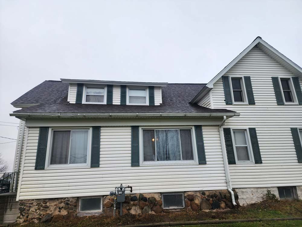 A white house with black shutters and a roof.