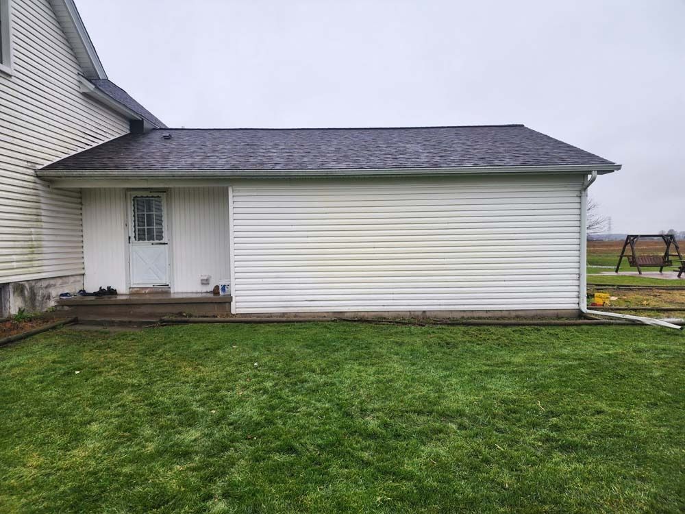 A white house with a black roof is sitting on top of a lush green lawn.
