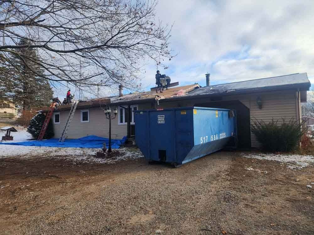 A large blue dumpster is parked in front of a house.