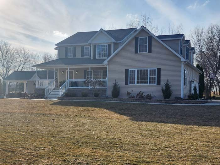 A large house with a large porch is sitting on top of a lush green field.