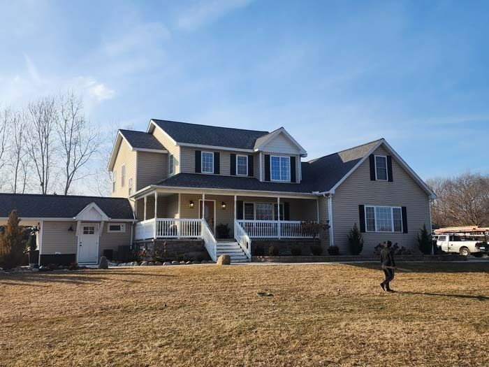 A man is walking in front of a large house with a porch.