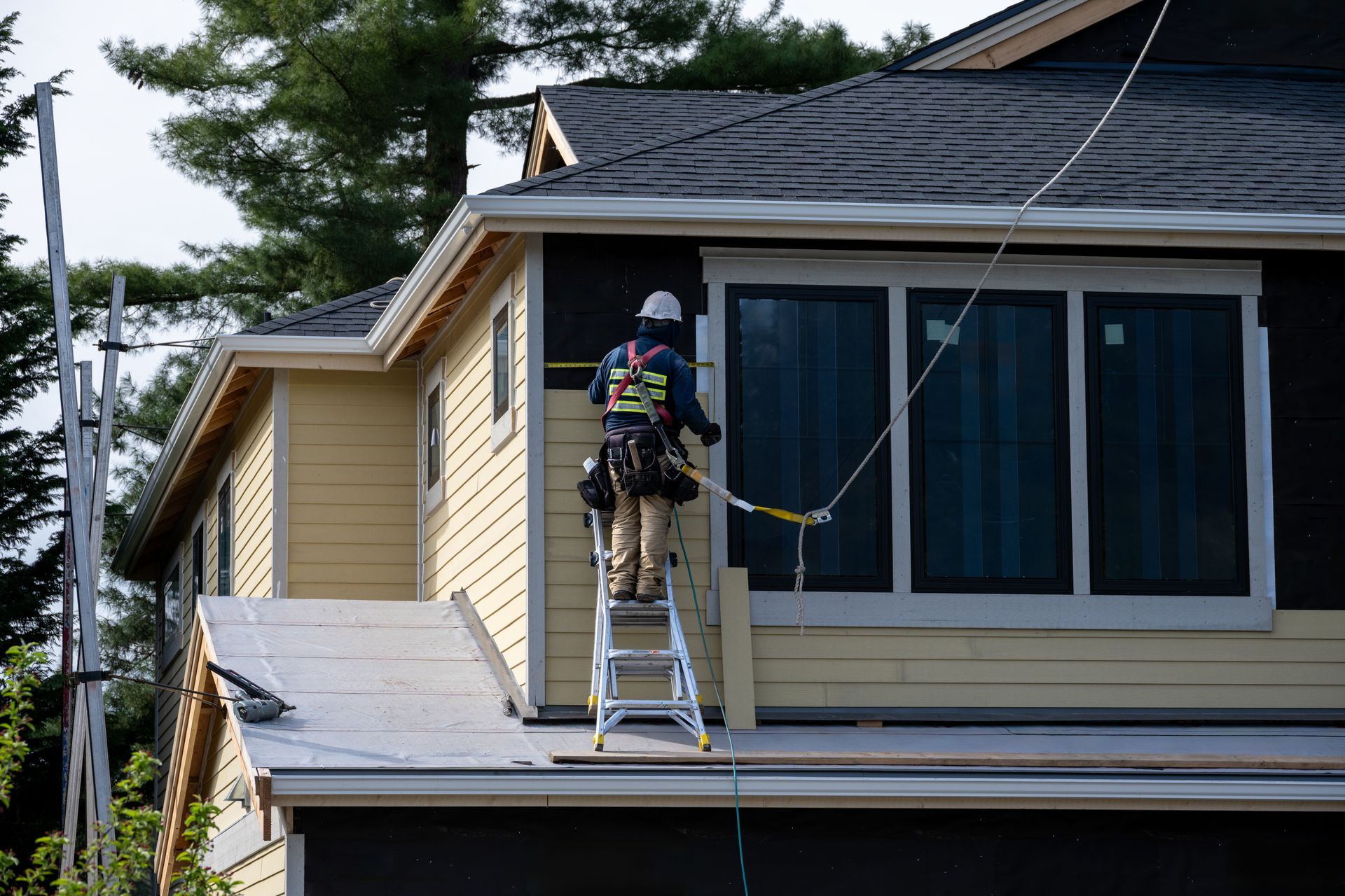 Worker on a ladder measuring or installing exterior trim around windows on a house. Worker on a ladder measuring or installing exterior trim around windows on a house.