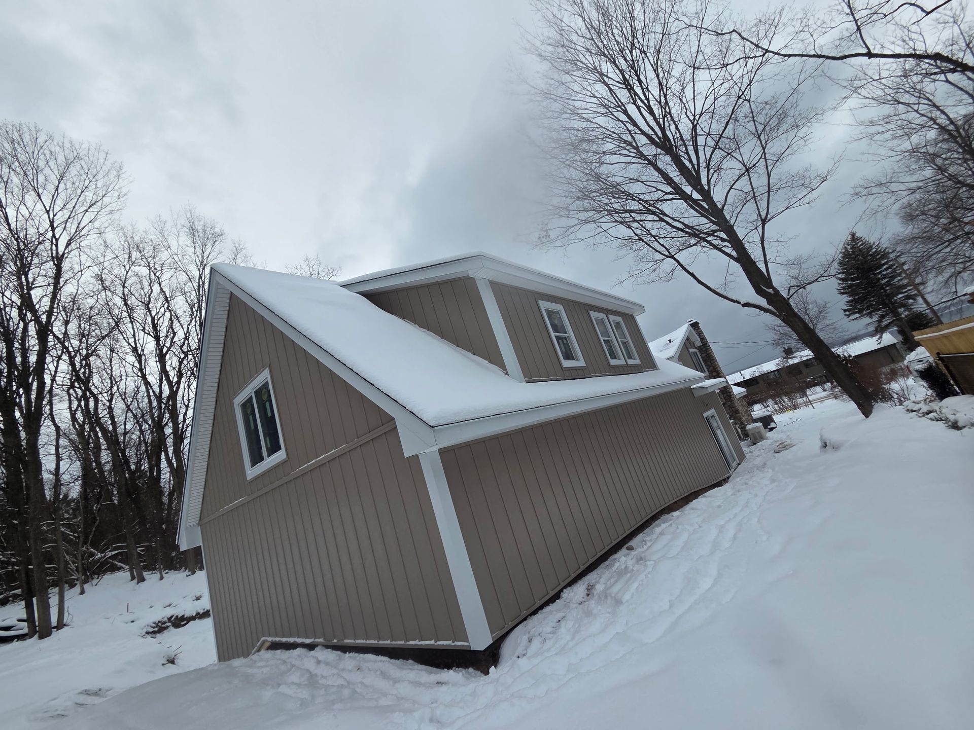 Tan building with snow-covered roof and siding, on a snowy hill, under a cloudy sky.