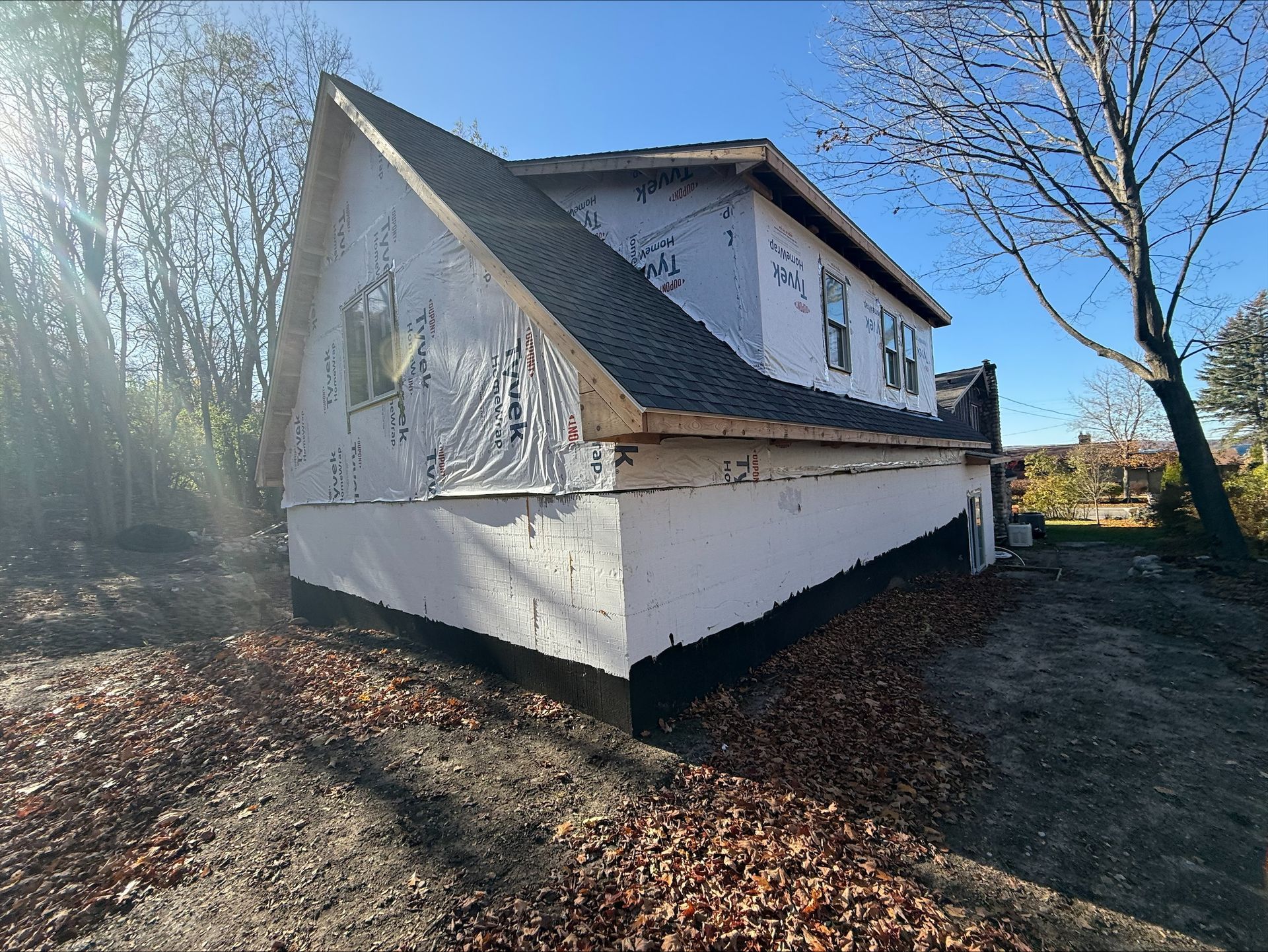 Building under construction with white siding and dark roof, leaves on the ground.