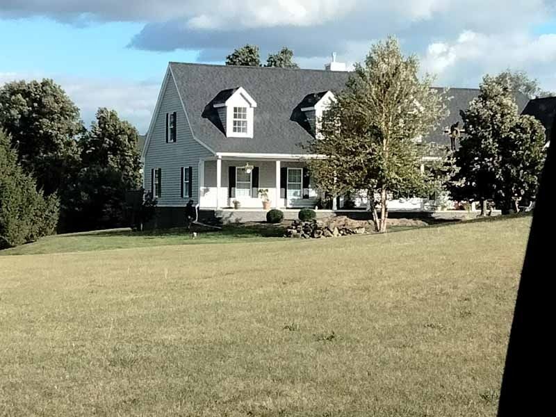 A large white house with a gray roof sits in the middle of a grassy field