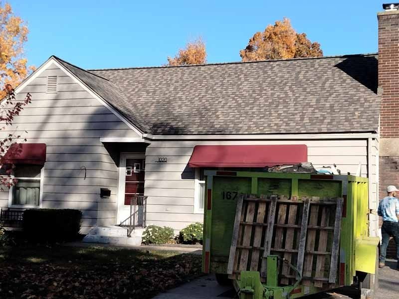 A green dumpster is parked in front of a house
