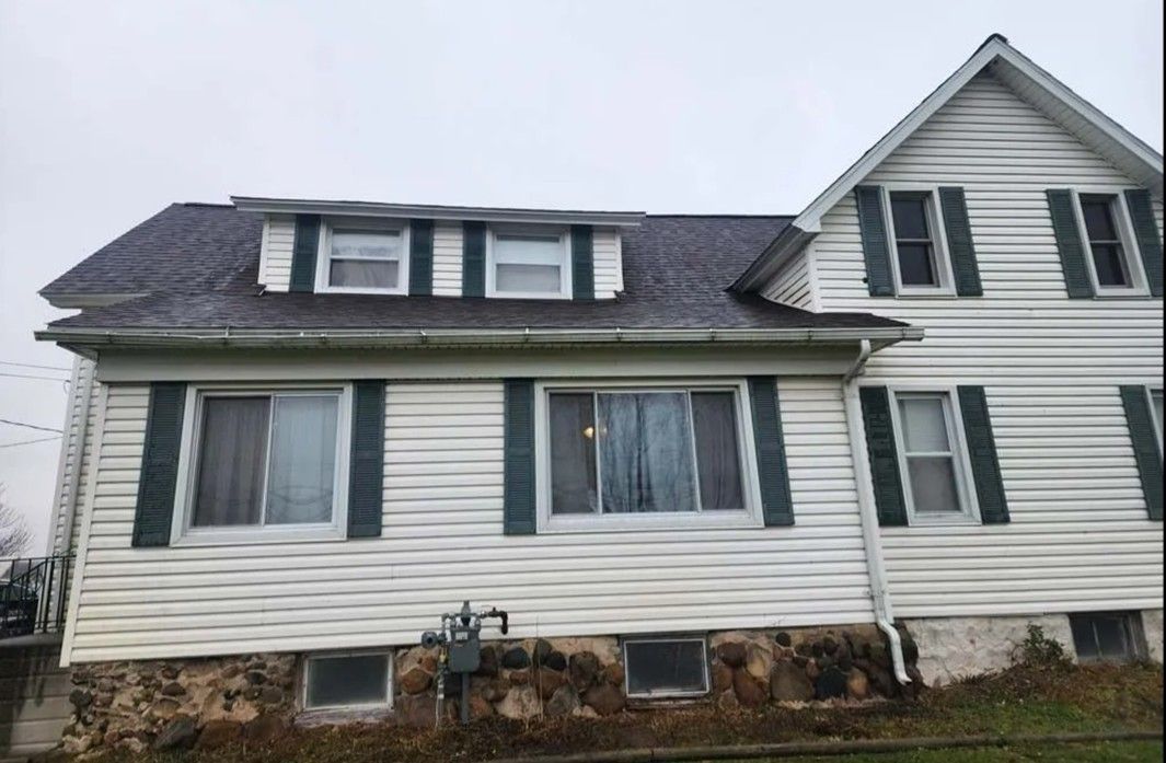 Front view of a white house with green shutters, dormer windows, and stone foundation. Front view of a white house with green shutters, dormer windows, and stone foundation.