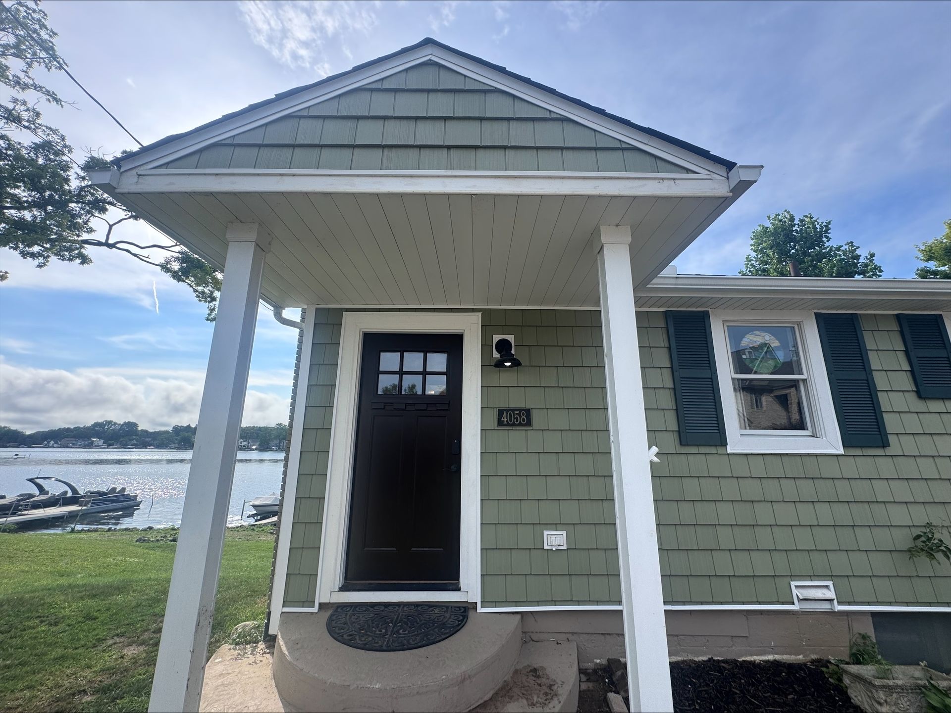 Green house with porch overlooking water, boats, and green grass.
