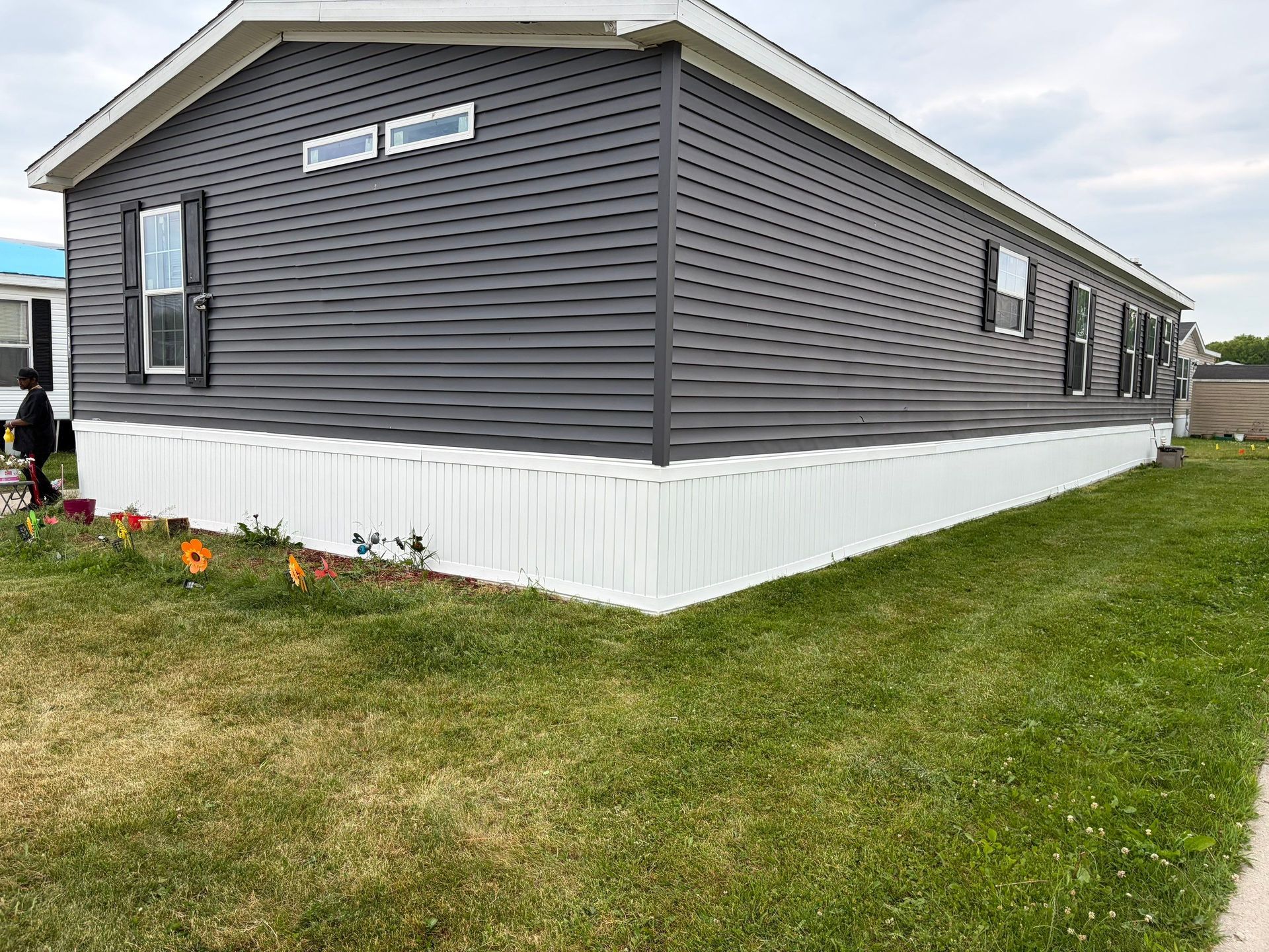 Gray mobile home with white skirting on a grassy lot, viewed from the corner.