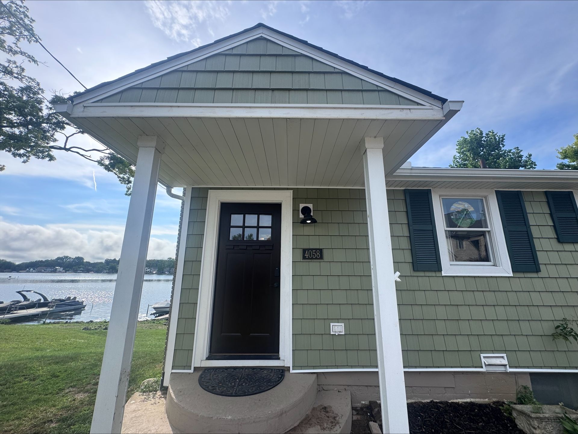 Small green house with a covered entrance, black door, and view of a lake in the background.