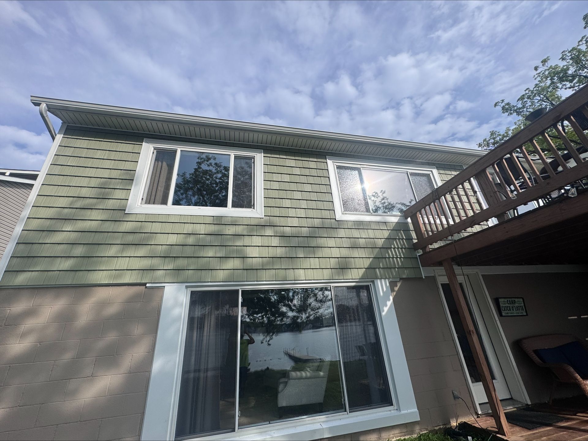 Green-sided house with white-framed windows and a wooden deck under a blue sky.