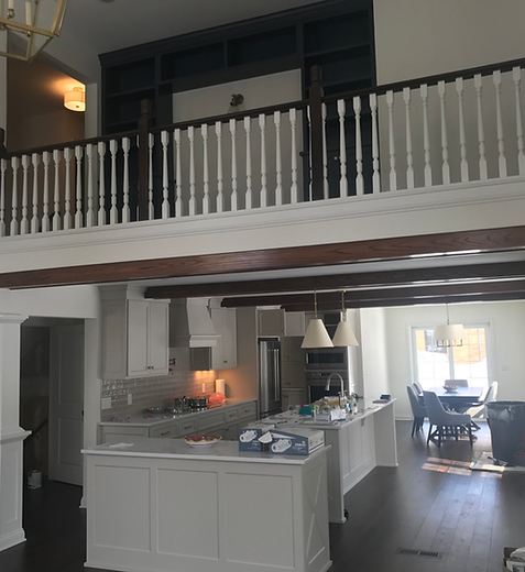 Open-concept home interior with white kitchen island, loft railing, and dining area in the background