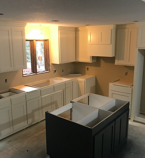 Kitchen under renovation with white cabinets, black island base, and unfinished floor