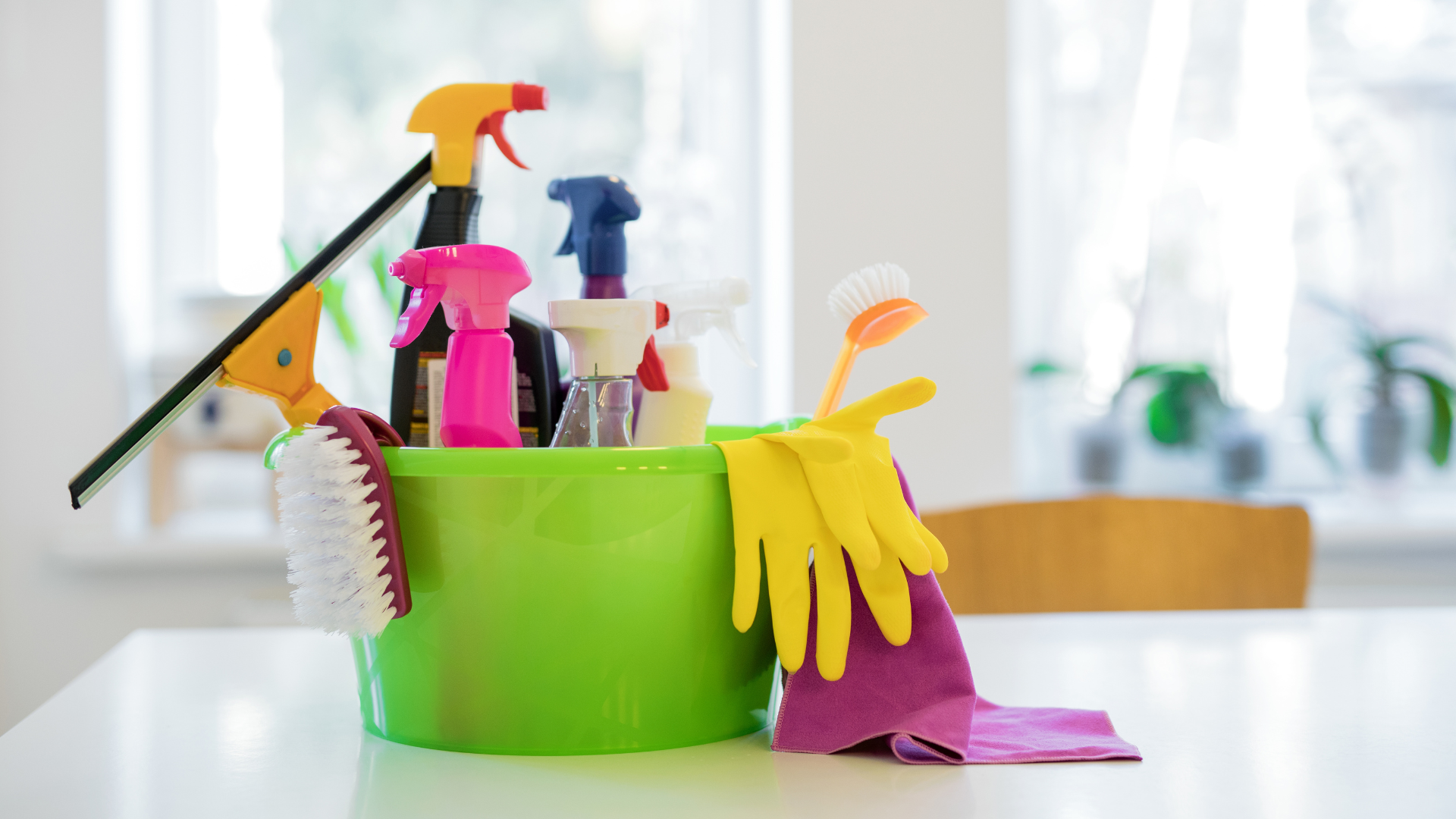A green bucket filled with cleaning supplies and gloves on a table.