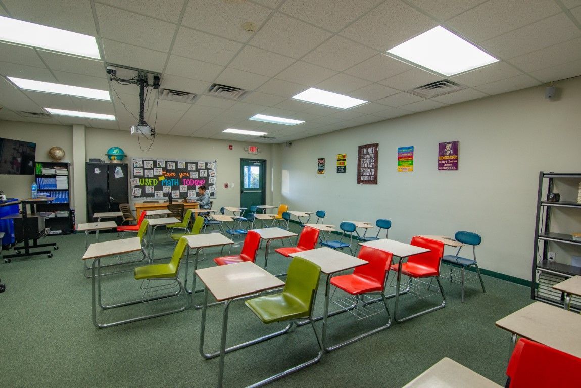 A classroom with colorful chairs and desks, various posters on the wall, and overhead projector.