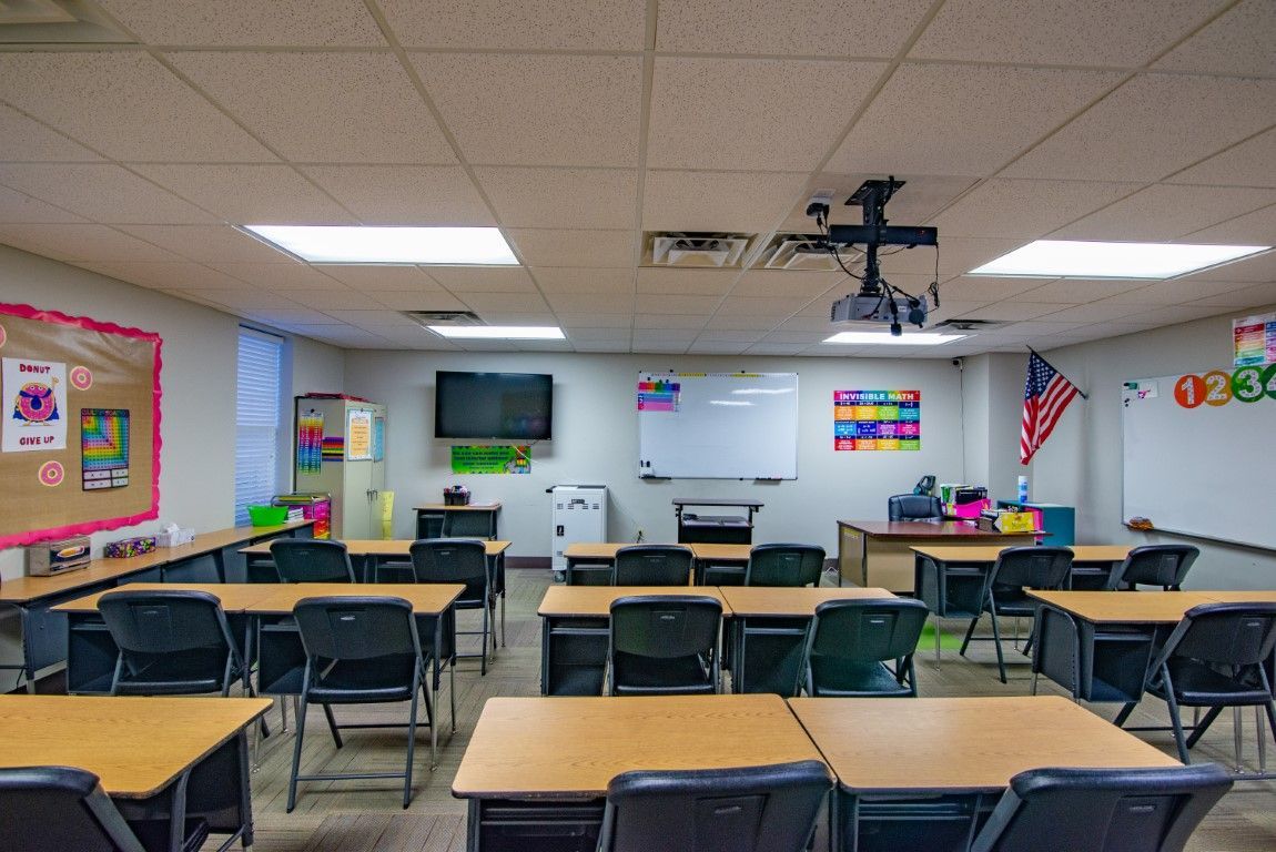 Empty classroom with desks, black chairs, and a whiteboard. American flag on wall.