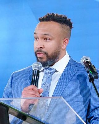 Man in a blue suit speaks into a microphone at a podium.