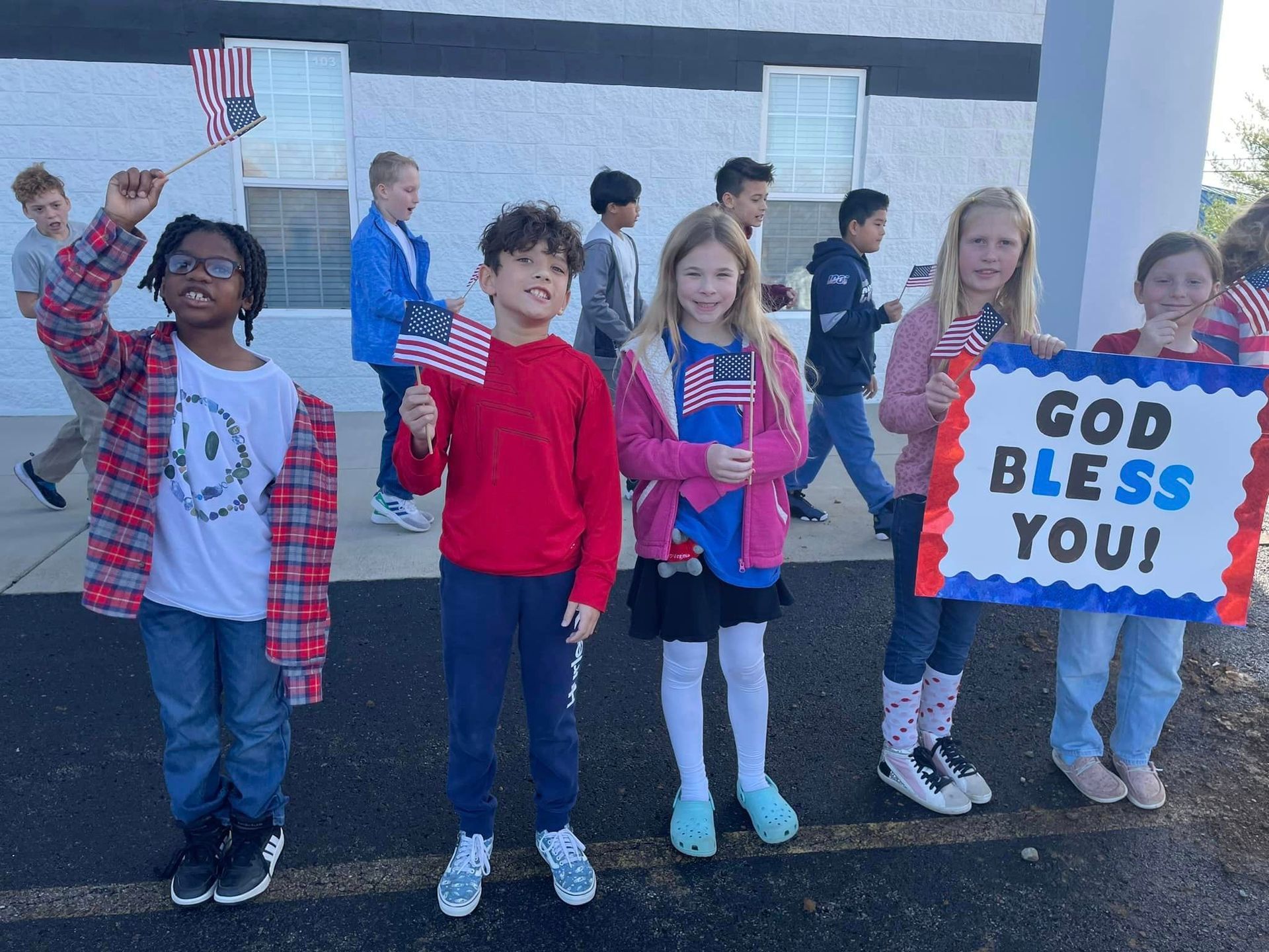 Children waving American flags and sign, cheering outdoors.
