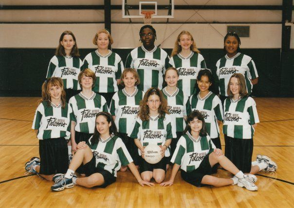 A youth soccer team in green and white jerseys poses on a basketball court.