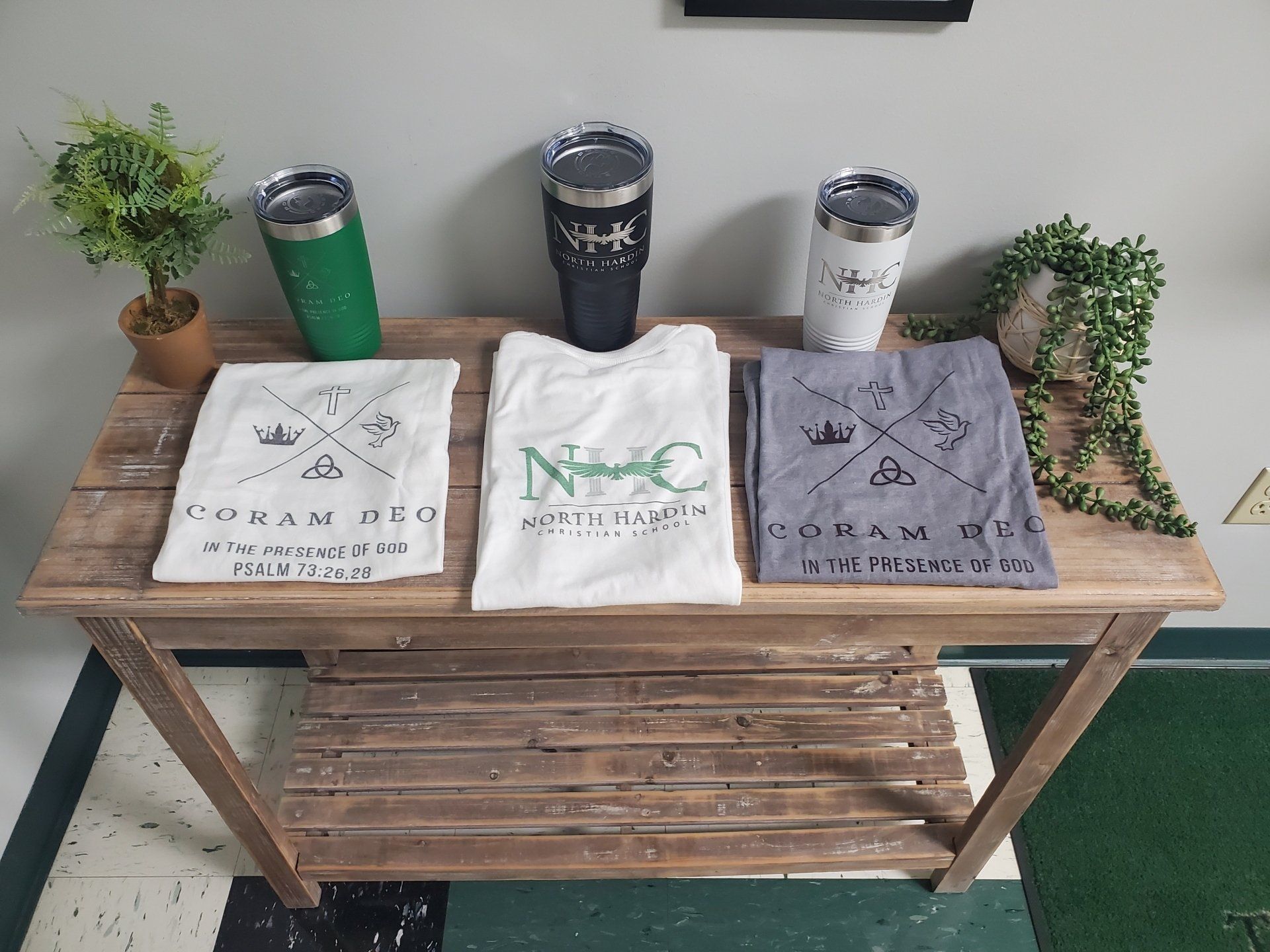 T-shirts, tumblers, and plants displayed on a rustic wooden table.
