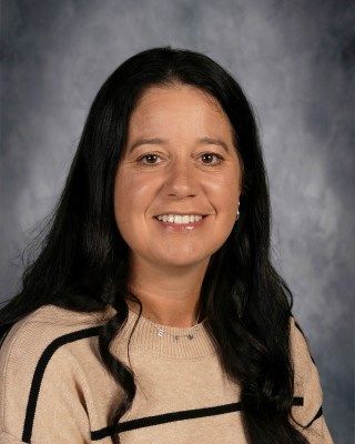 Woman with long dark hair smiles, wearing a tan sweater with black stripes.