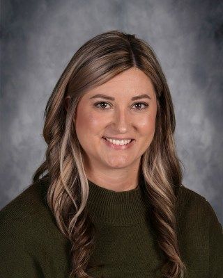 Woman with brown hair and highlights, smiling, wearing a green sweater.