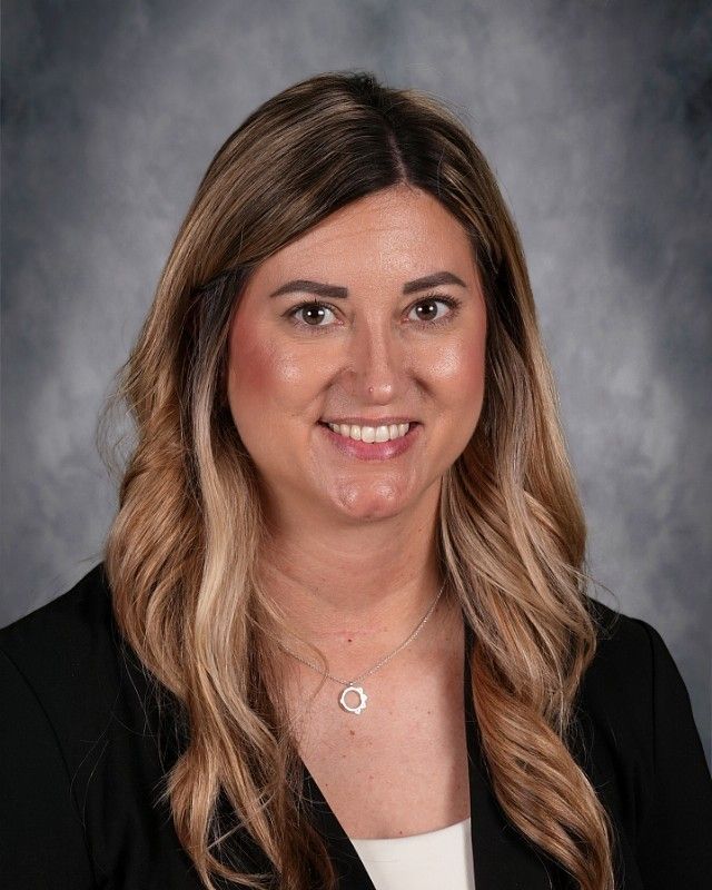 Woman with light brown hair and a smile, wearing a dark green sweater.