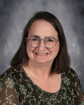 Woman with glasses and a floral shirt smiling.