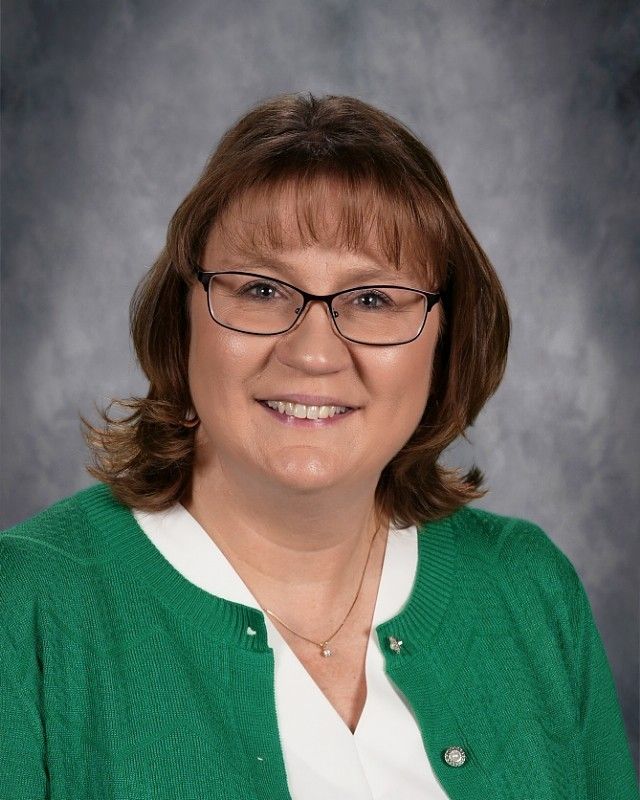 Woman with long wavy brown hair smiling, wearing a denim jacket.