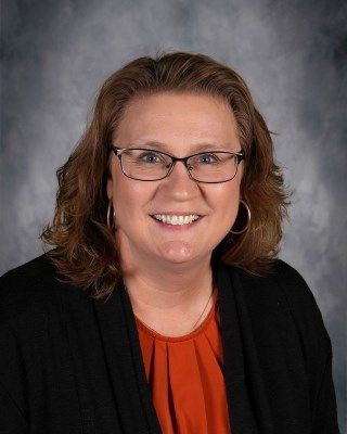 Woman with glasses smiling, wearing orange shirt and black cardigan.