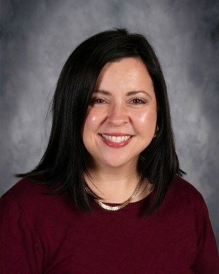 Woman with dark hair and a maroon shirt, smiling.