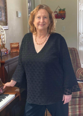 Woman in black top with piano in a living room, smiling.