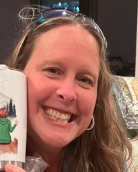 Woman smiling, holding a mug with a drawing of a person in green coat near a city landscape.