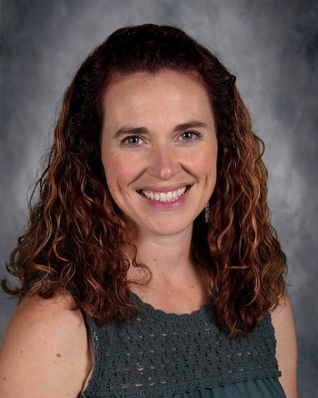 Smiling woman with brown curly hair and a denim jacket.