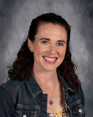 Smiling woman with brown curly hair and a denim jacket.